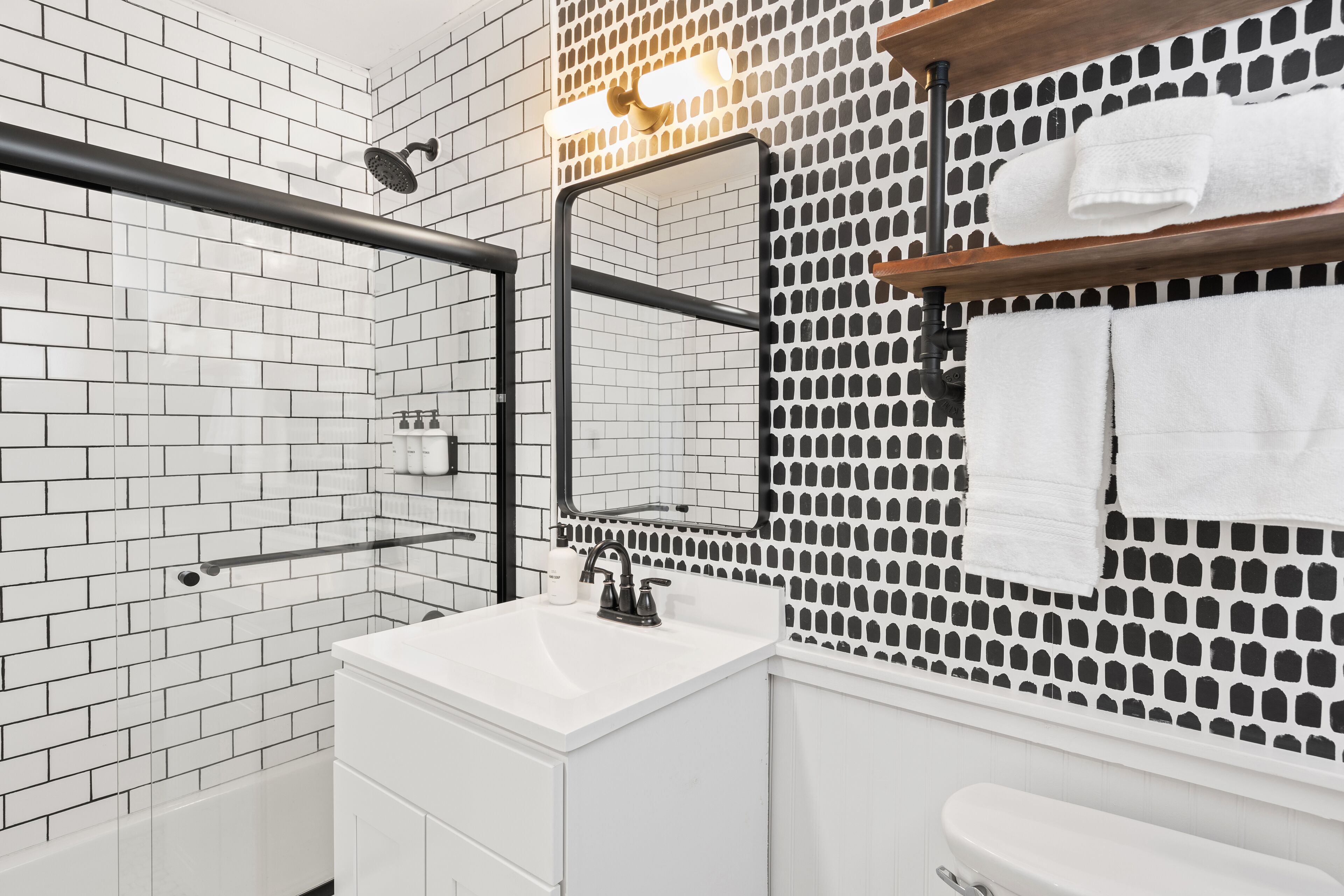 Een moderne badkamer met witte metro tegels, een douchecabine met glazen wanden, een witte wastafel en een spiegel met een zwarte omlijsting.
