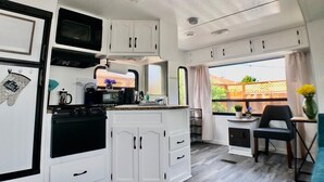 Cocina compacta con armarios blancos, microondas y estufa. Cuenta con un pequeño comedor con una silla y una mesa.