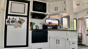 Una cocina compacta con armarios blancos, microondas, estufa y cafetera.