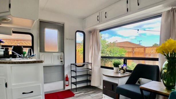 Cocina compacta con armarios blancos, una pequeña encimera y una ventana con cortinas.