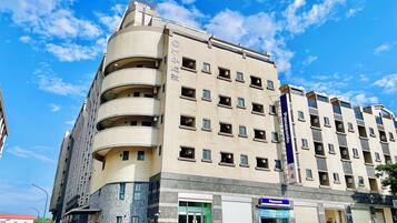 Un hotel de varios pisos con fachada curva, múltiples balcones y una tienda Panasonic en la planta baja.