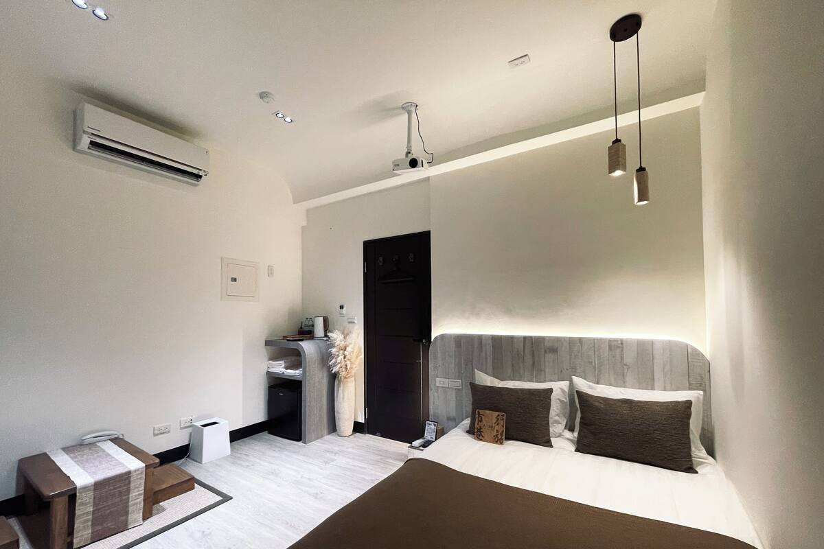 A modern bedroom with a large bed, bedside tables, an air conditioning unit, and a desk with a chair.
