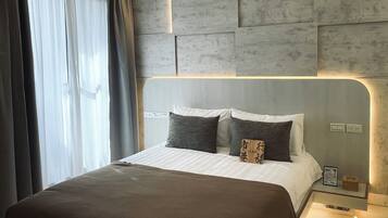 Una habitación de hotel moderna con una cama grande, cabecera con iluminación integrada y una mesita de noche con lámpara.