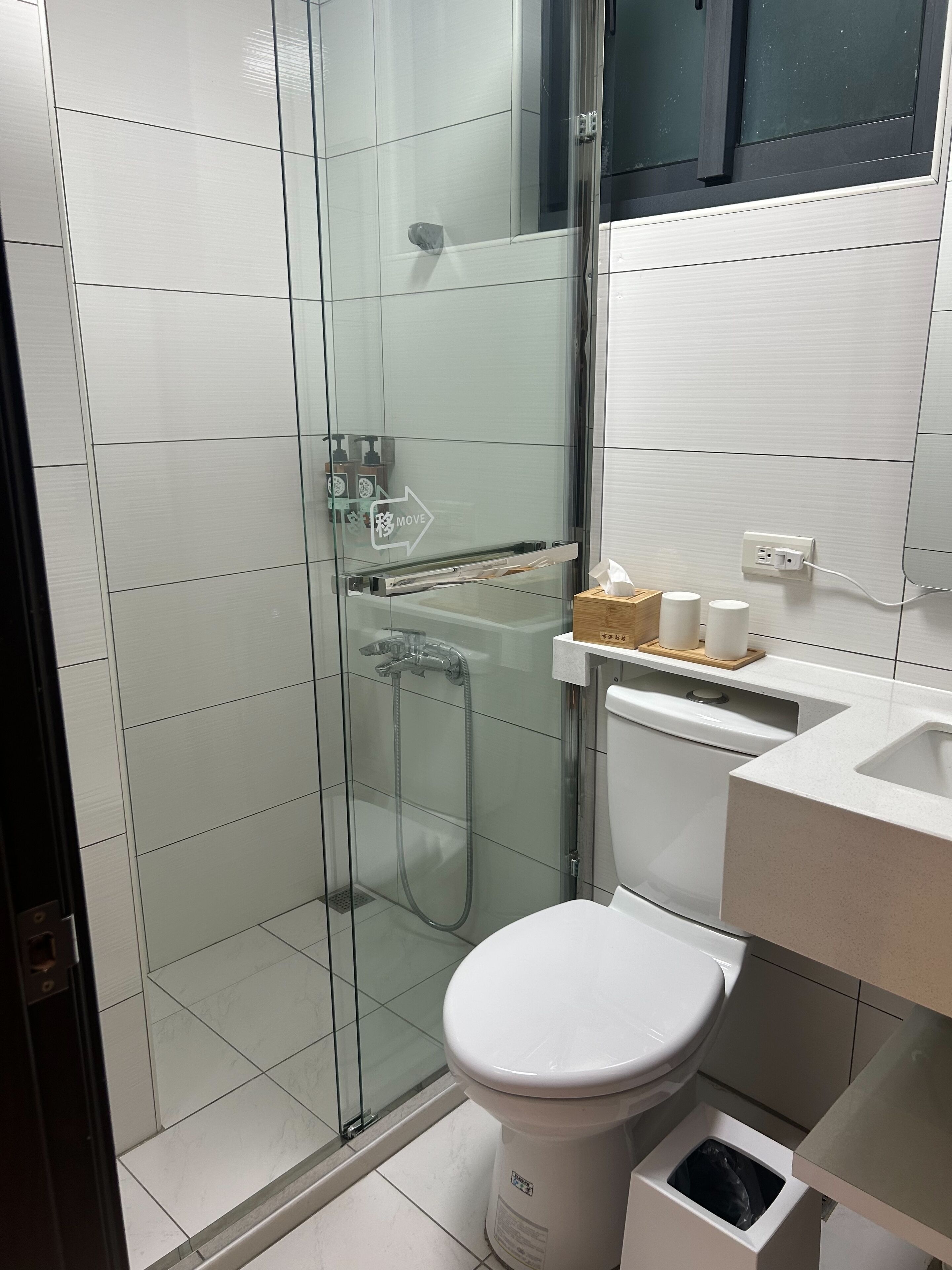 Un baño moderno con ducha de vidrio, inodoro blanco y lavamanos con bandeja de madera.