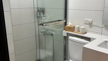 Un baño moderno con ducha de vidrio, inodoro blanco y lavamanos con bandeja de madera.