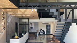 Un espace d’accueil moderne comprenant un comptoir de réception en bois, un coin salon avec des canapés en cuir, un escalier et une œuvre d’art fixée au mur.