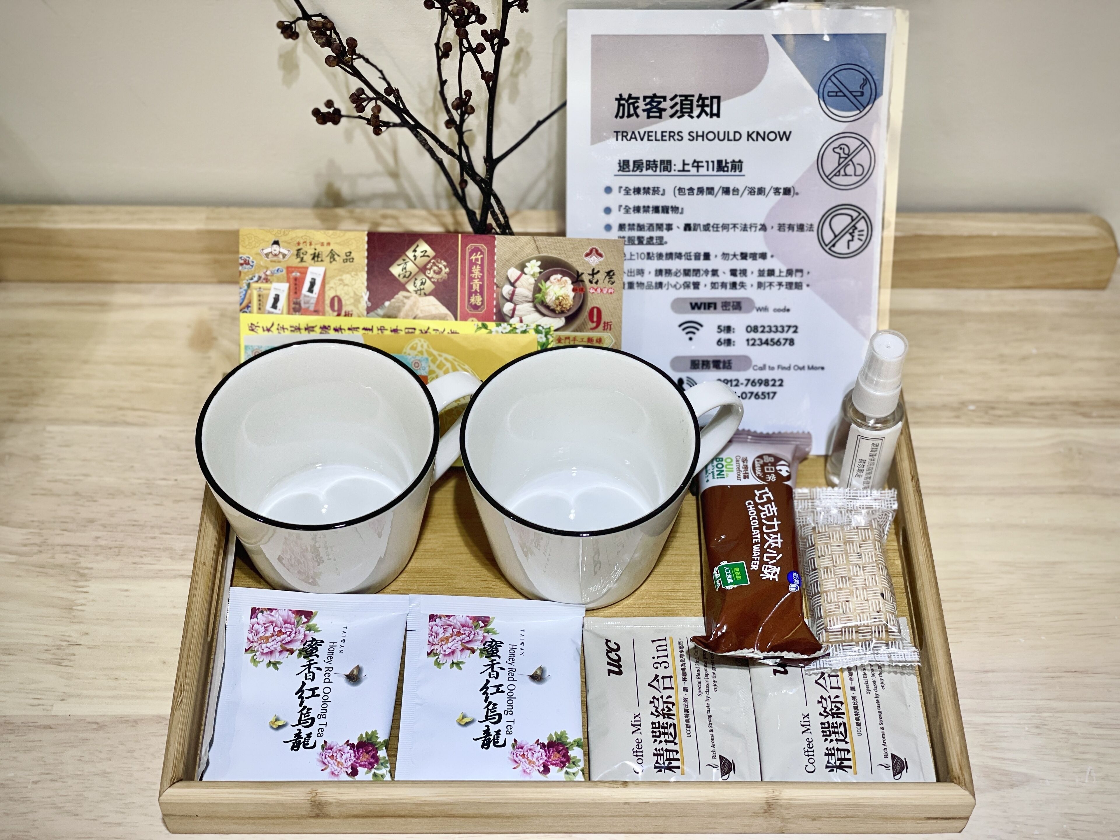A tray with two white cups, a box of tea, a bottle of lotion, and a sign with travel information.