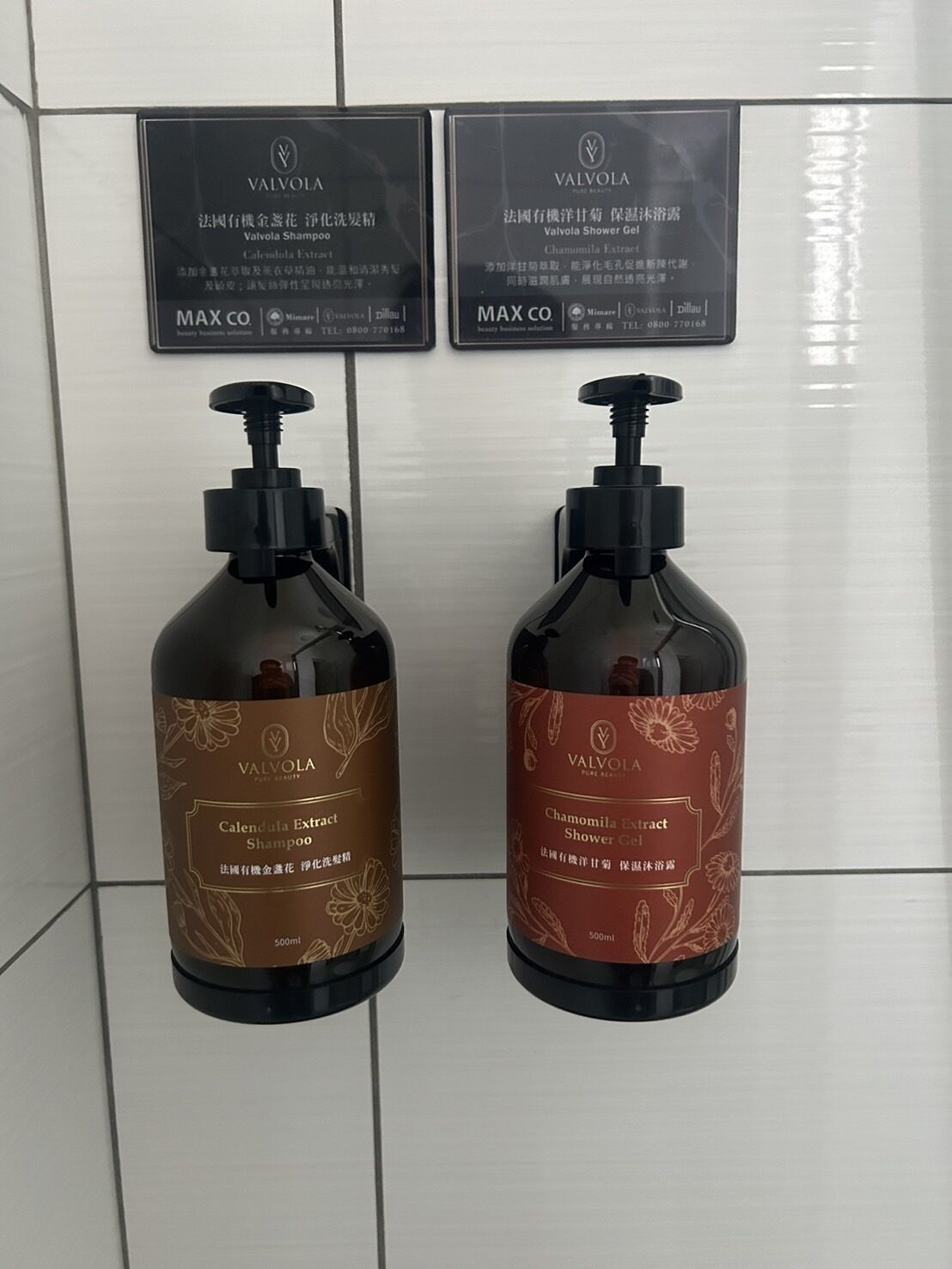 Dos botellas de champú y gel de ducha Valvola, cada una con capacidad de 500 ml, sobre una pared de azulejos.
