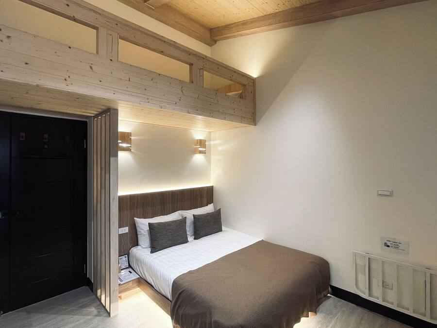Ein Schlafzimmer mit Bett, Holzbalkendecke, weißer Wand und Heizkörper.