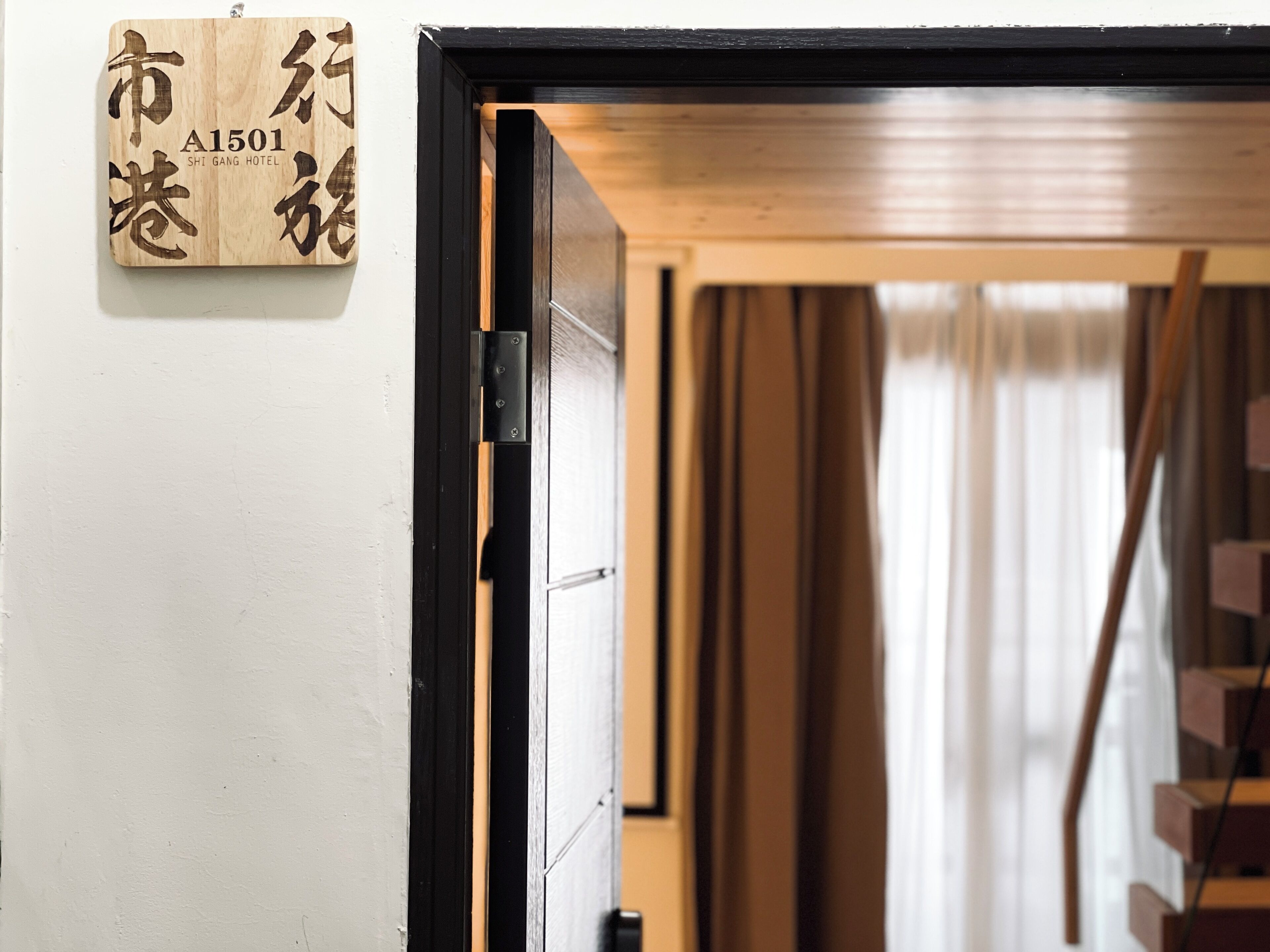 A wooden sign with Japanese characters and a hotel name, a black door frame, and a staircase leading to a room.