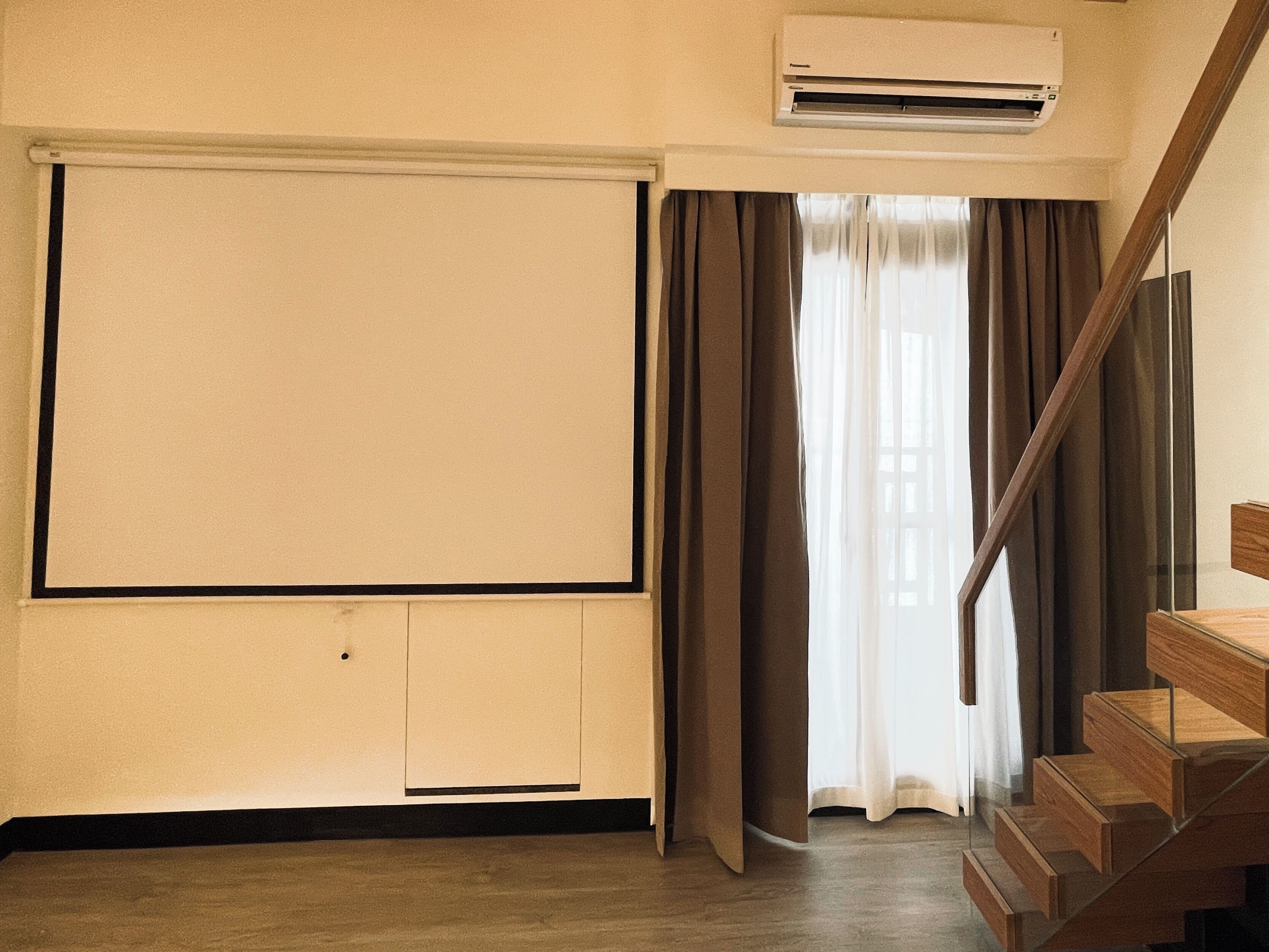Una habitación con un ventanal grande, una escalera de madera y un equipo de aire acondicionado.