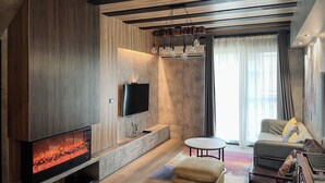 Un salon moderne avec un téléviseur à écran plat, une cheminée, un canapé et une petite table ronde.