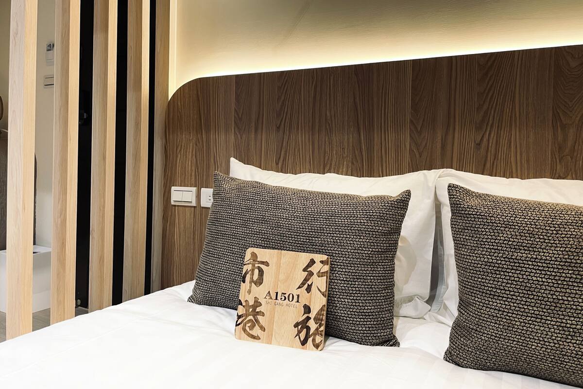 A neatly made bed with a wooden headboard, two patterned pillows, and a wooden plaque with text.