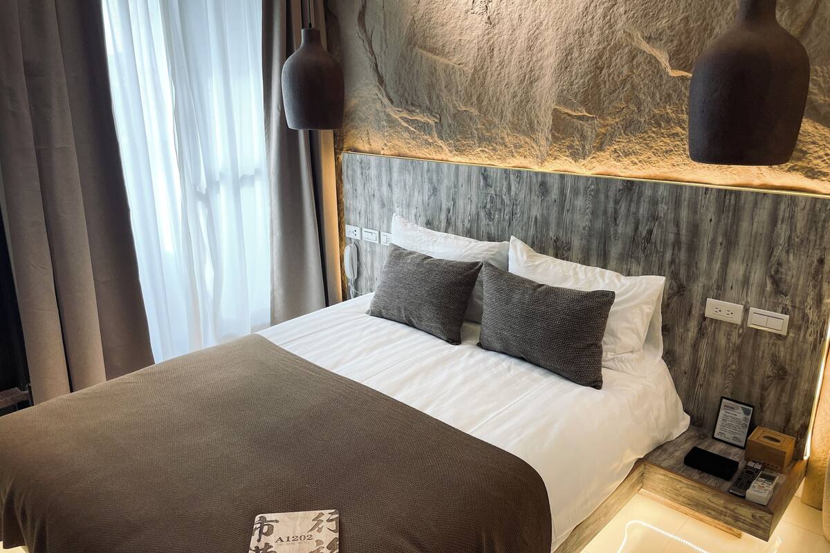A neatly made bed with a white and brown bedspread, two pillows, and a bedside table with a remote control and a tissue box.