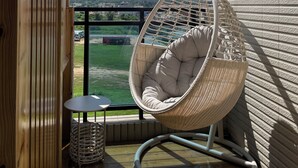 Un fauteuil suspendu sur un balcon, offrant une vue sur un paysage verdoyant et des collines lointaines.