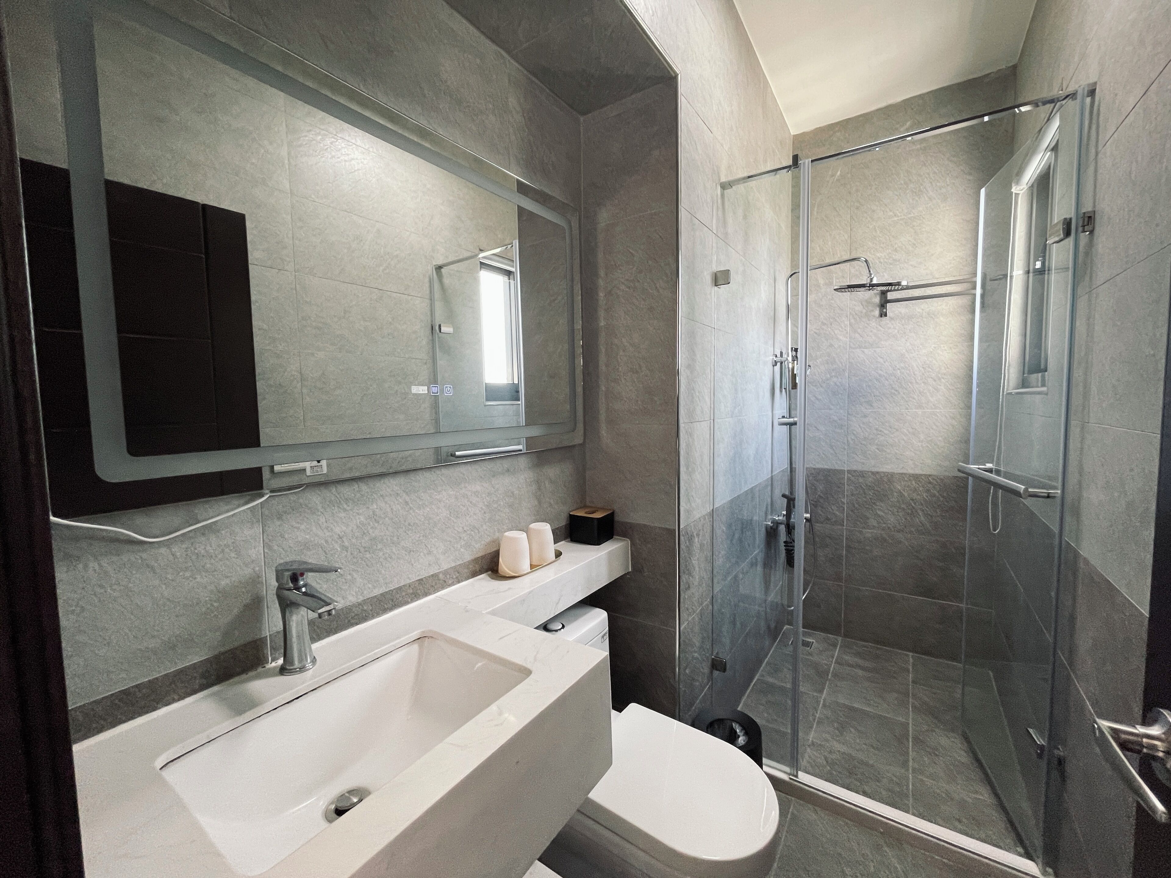 A modern bathroom with a large mirror, a sink, a toilet, and a glass-enclosed shower.