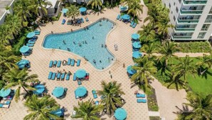 Vista aérea de um resort com piscina, espreguiçadeiras e palmeiras.
