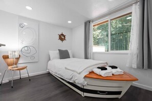 Una camera da letto moderna con un letto, una sedia, una finestra con tende e una parete decorata con arte astratta e una ruota di timone.