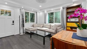 A modern living room with a sectional sofa, a glass coffee table, and a wooden dining table. - Mount Hermon Redwood Retreat! (Felton)