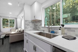Une cuisine moderne dotée d’une grande fenêtre, de meubles blancs et d’un dosseret carrelé de couleur grise.