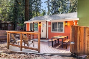 A small cabin with a deck, a wooden fence, and a bench.