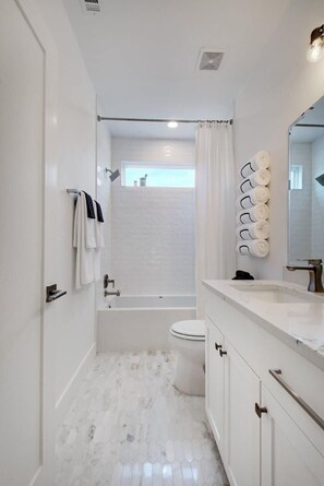A modern bathroom with a white marble floor, a bathtub, a toilet, and a vanity with a mirror.