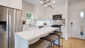 Une cuisine moderne dotée d’un grand îlot central, d’appareils électroménagers en acier inoxydable et d’un lustre contemporain.