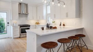 Une cuisine moderne avec des meubles blancs, un îlot central doté de tabourets, des appareils en acier inoxydable et un éclairage suspendu.