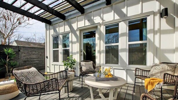 Une terrasse couverte, aménagée avec des meubles en osier, une table ronde et un panier de fruits.