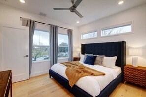 Un dormitorio moderno con una cama grande, un ventilador de techo y dos ventanas con cortinas.