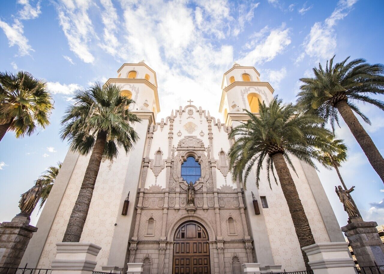 A church with two bell towers, a central entrance, and palm trees.