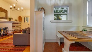 Un salon chaleureux avec une cheminée, un canapé, une table à manger en bois et une fenêtre donnant sur des palmiers.