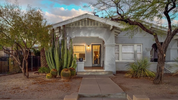 Une maison à deux étages avec un porche à l’avant, un garage et un jardin bien entretenu où poussent des cactus.