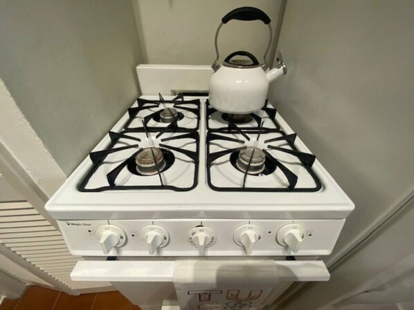 Una estufa de gas blanca con cuatro quemadores y una tetera encima.