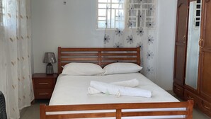 Una cama bien tendida con sábanas blancas, un cabecero de madera y una mesita de noche con una lámpara.