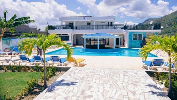 Un edificio de dos pisos con piscina, sillas de descanso y una zona de estar cubierta.