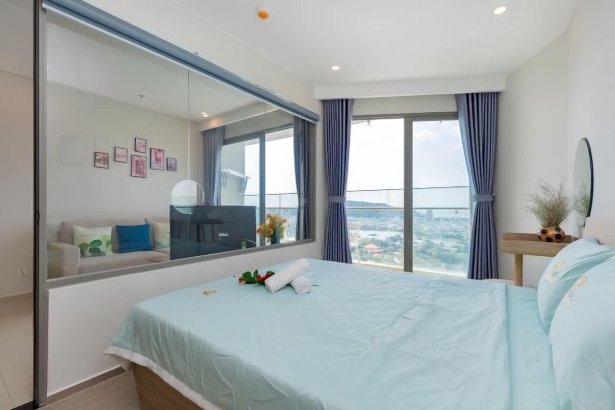 A bedroom with a large bed, a TV, a mirror, and a view of the city.