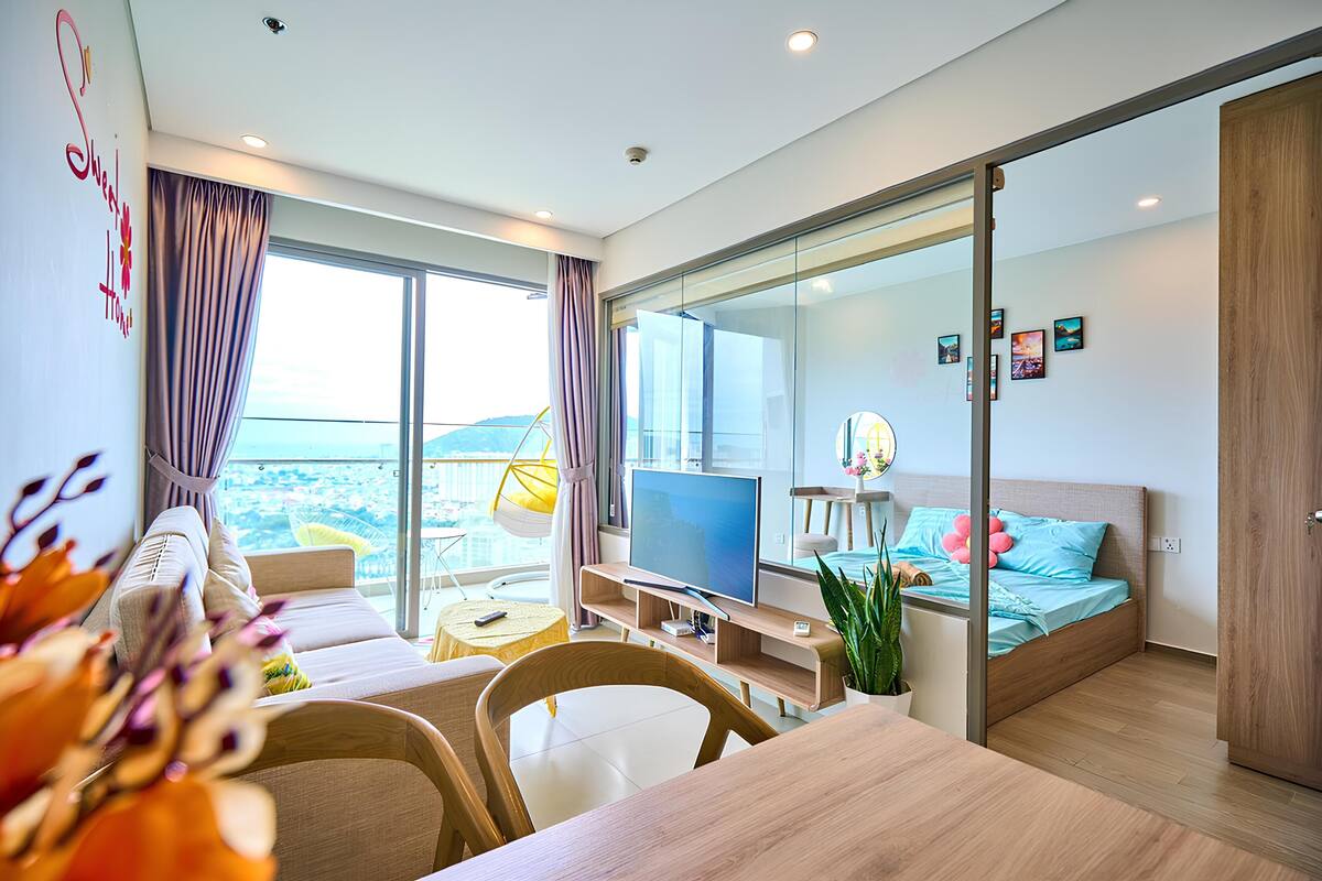 A modern hotel room with a balcony, a bed, a TV, and a dining area.