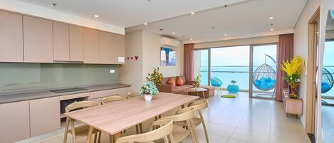 A modern living room with a dining area, large windows, and a view of the sea.