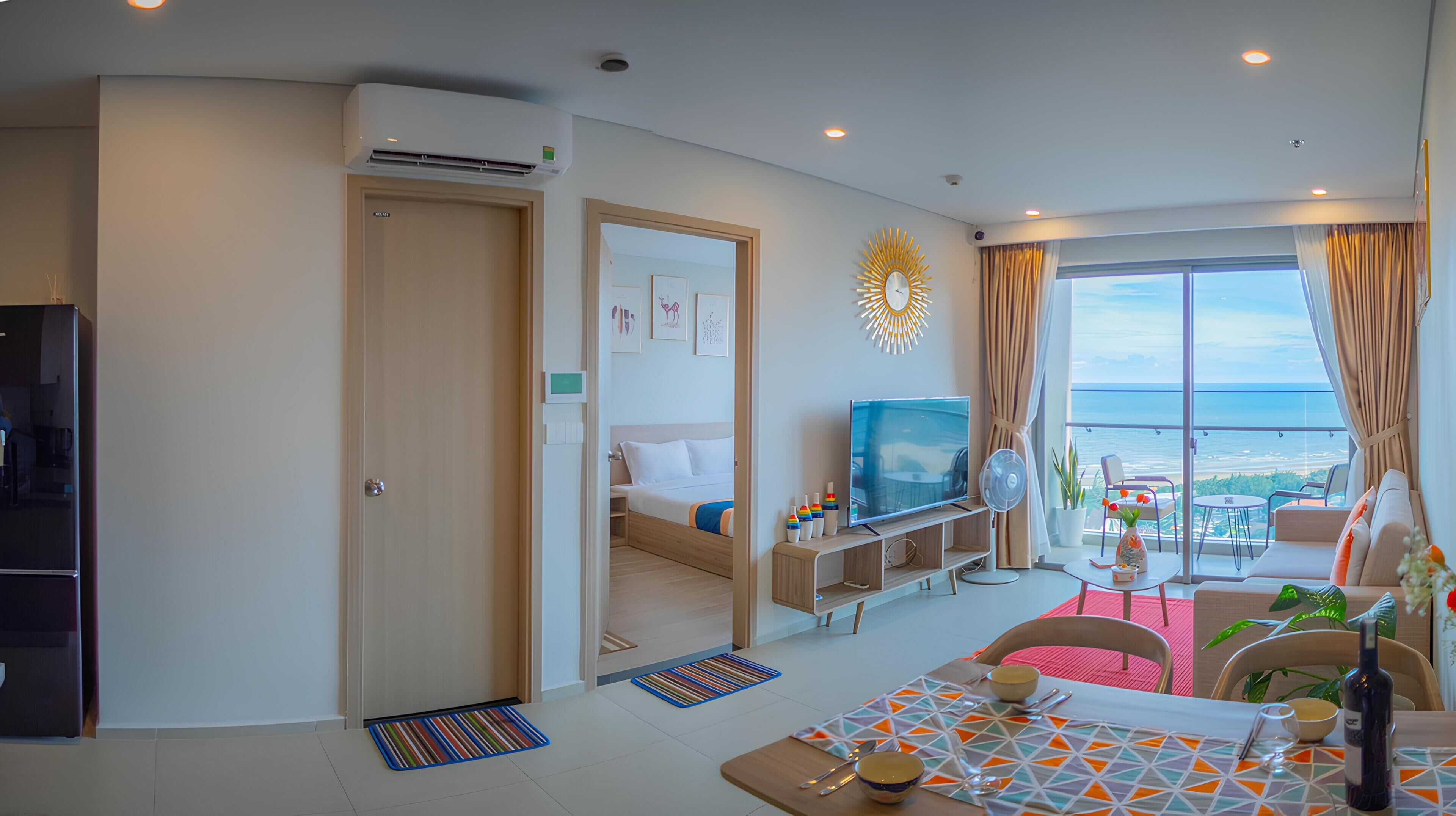 A modern hotel room with a balcony, a television, a dining area, and a bed.