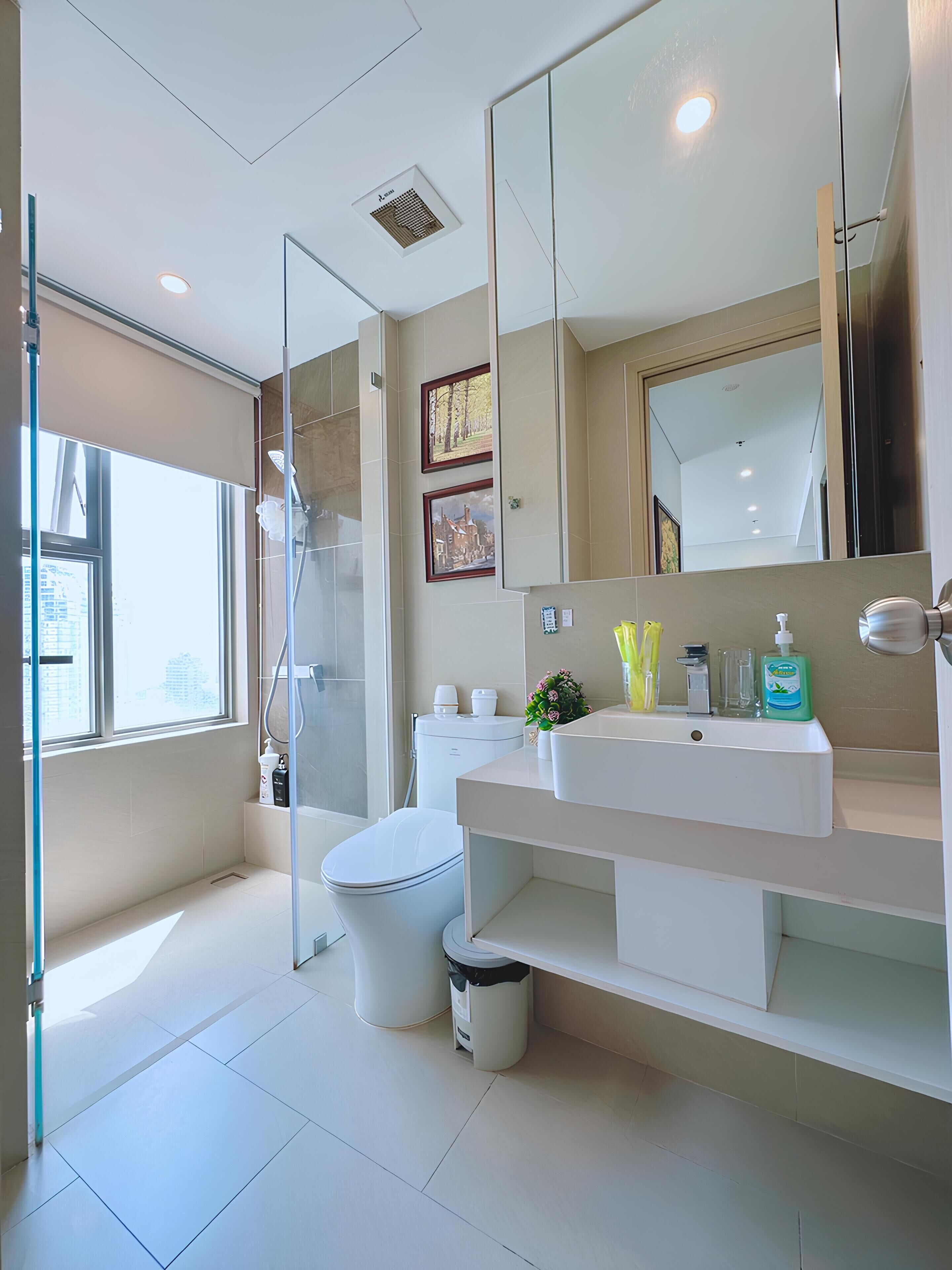 A modern bathroom with a glass shower enclosure, a white toilet, a large mirror, and a white sink with toiletries.