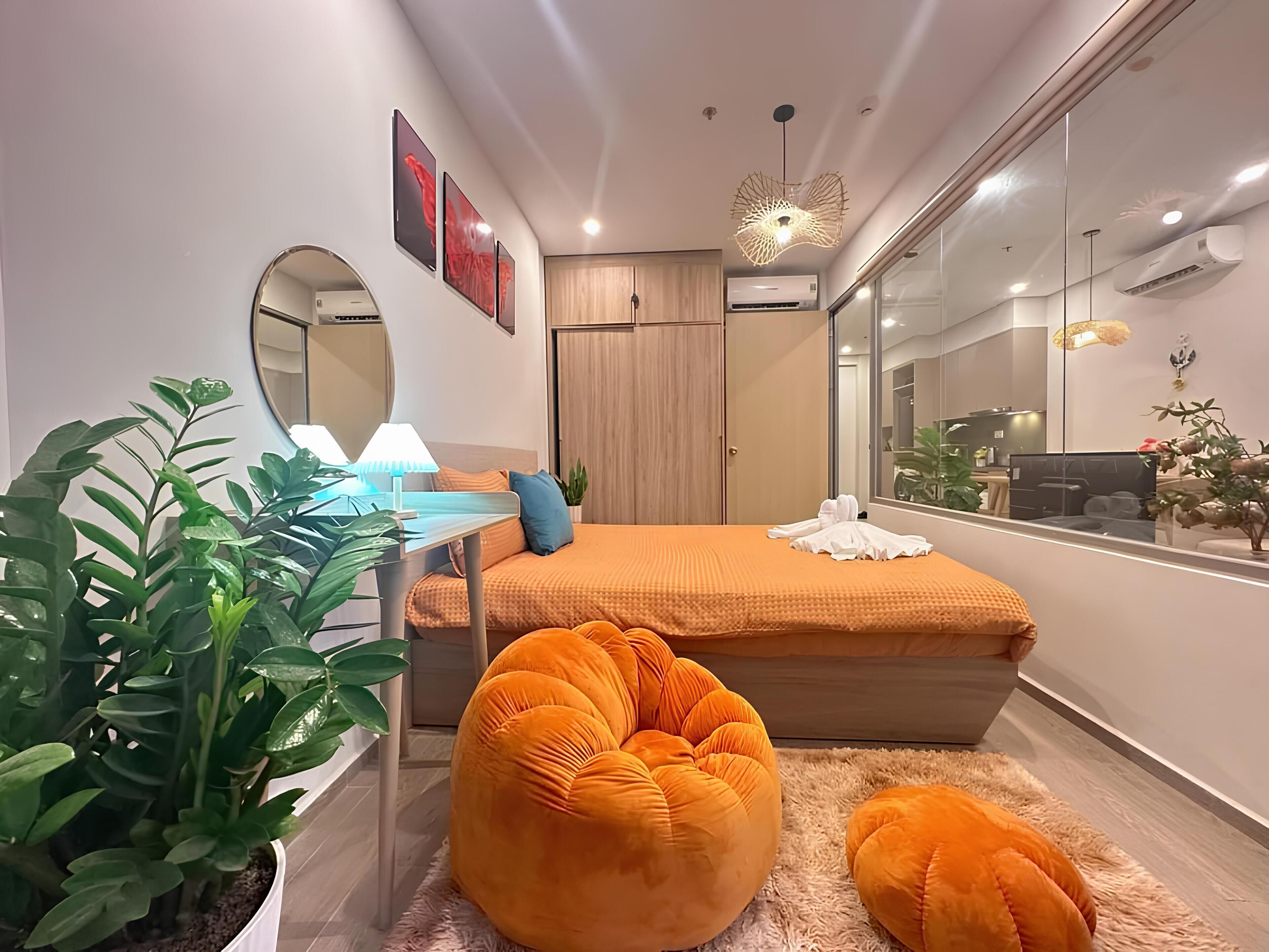 Une chambre à coucher moderne avec un lit, une table de chevet, une lampe, des plantes en pot et un grand miroir.