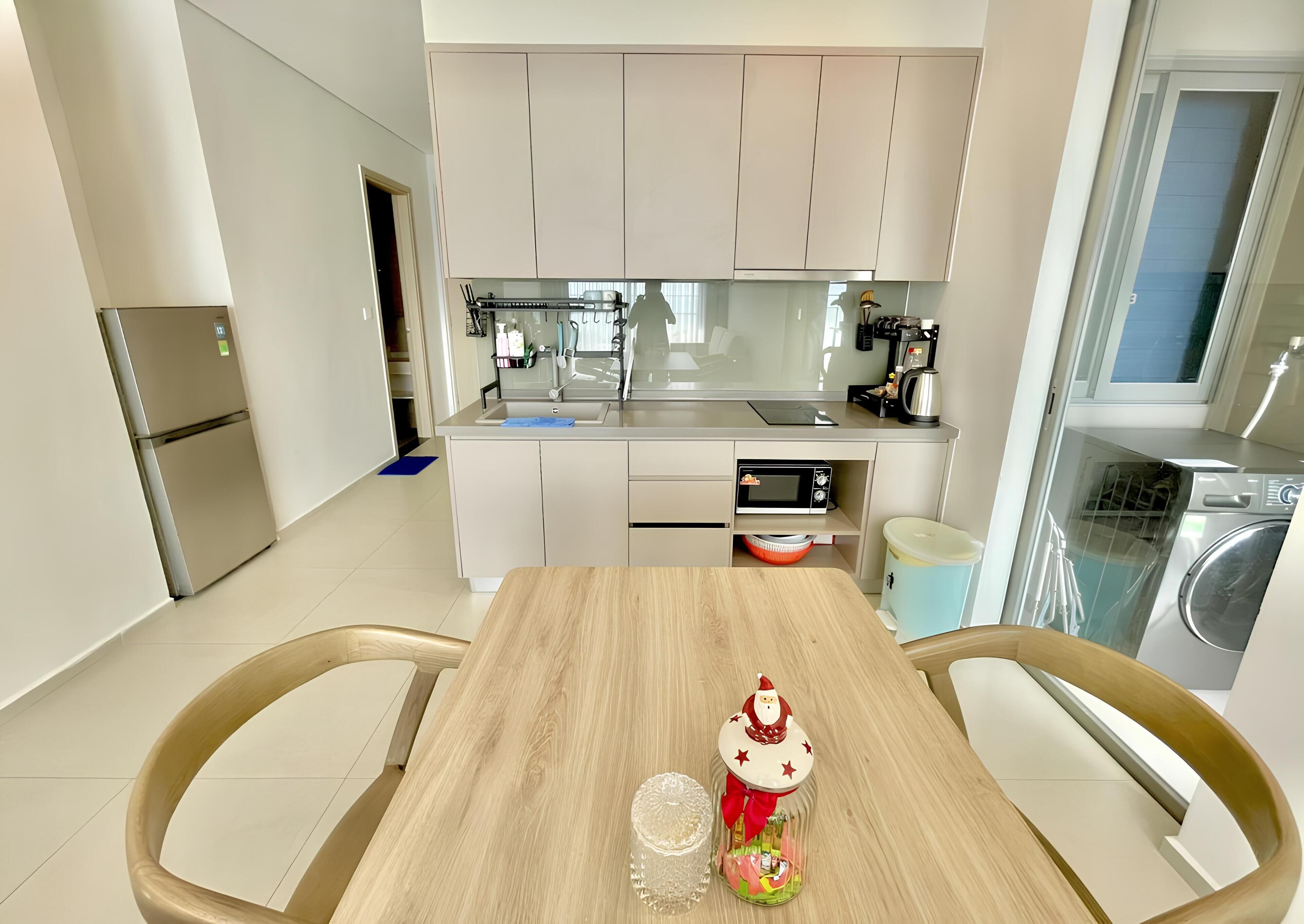 A modern kitchen with a central island, a built-in oven, and a microwave. There is a dining table with chairs and a decorative Santa ornament.
