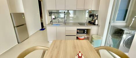 A modern kitchen with a central island, a built-in oven, and a microwave. There is a dining table with chairs and a decorative Santa ornament.