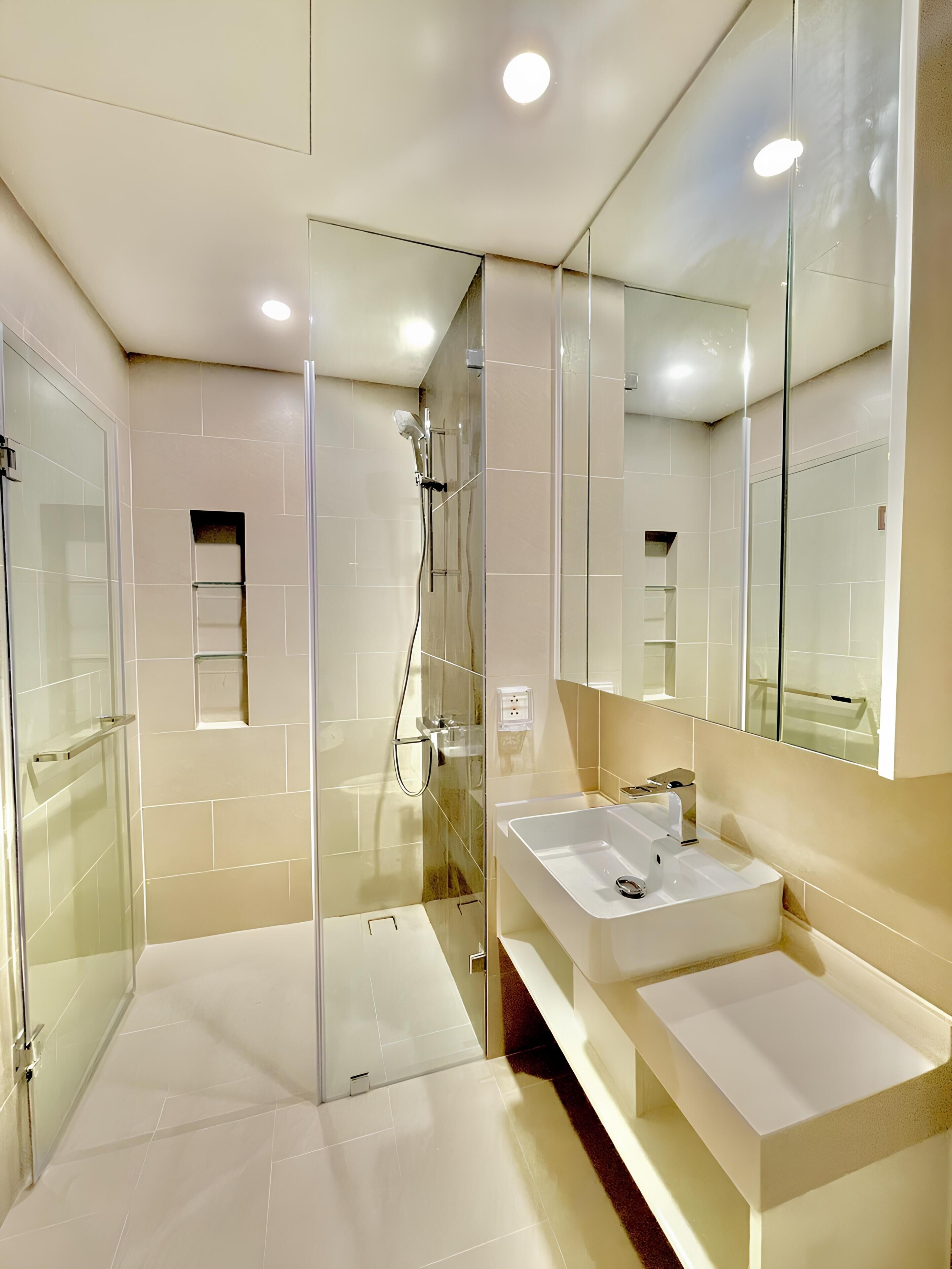 A modern bathroom with a glass-enclosed shower, a large mirror, and a white sink.