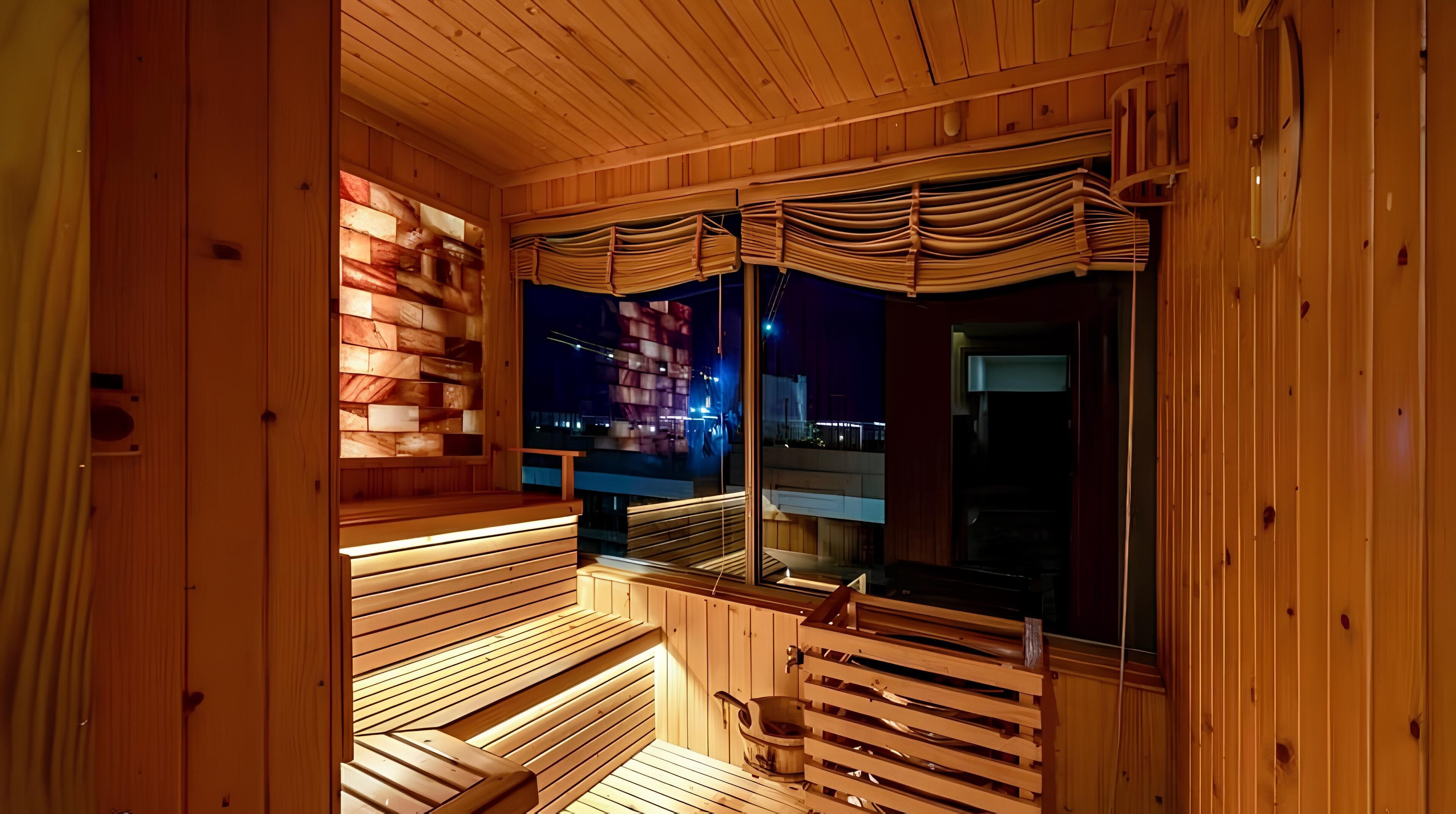 A wooden sauna with benches and a window overlooking a cityscape at night.