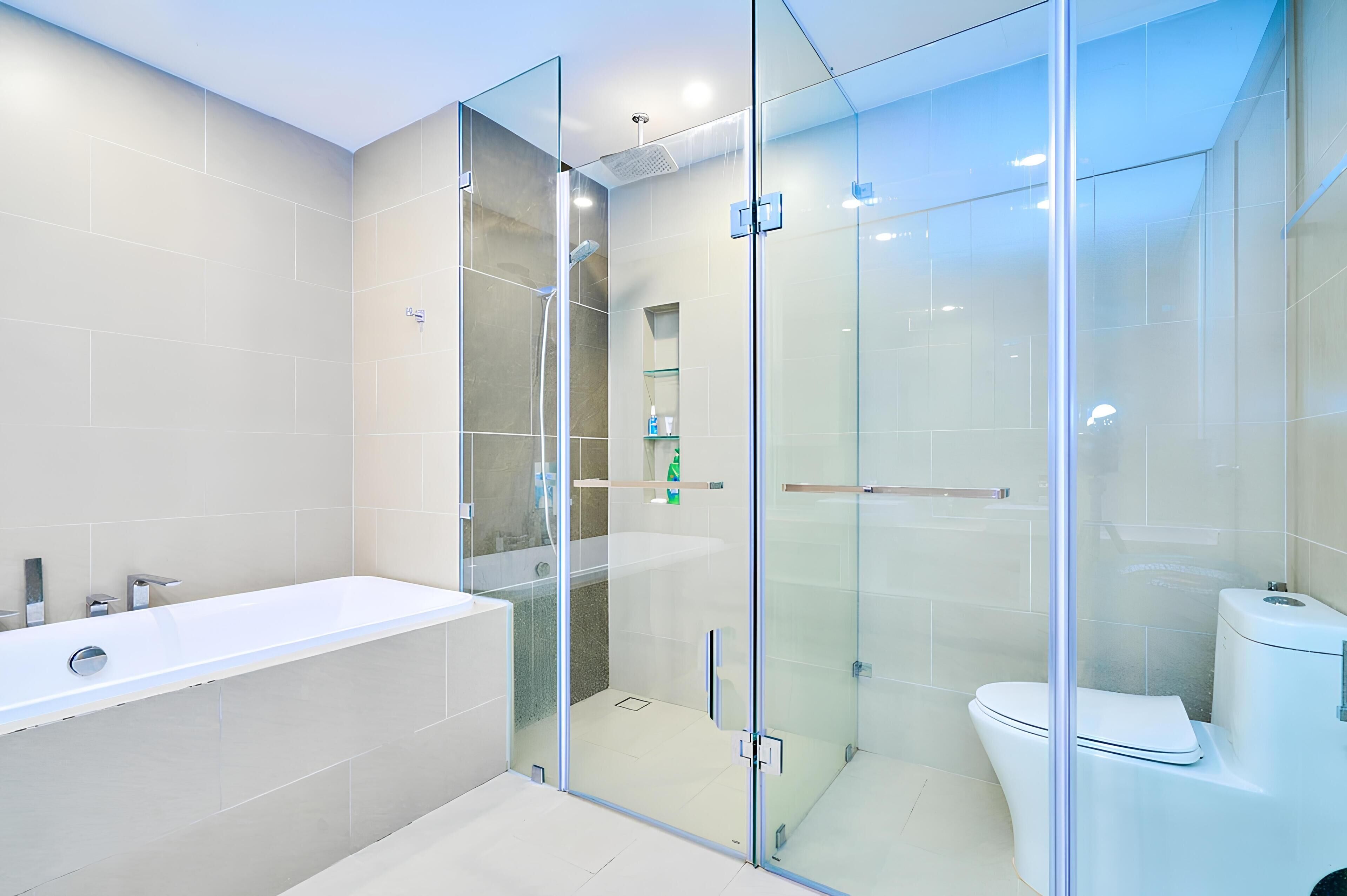 A modern bathroom with a glass-enclosed shower, a white bathtub, and a toilet.