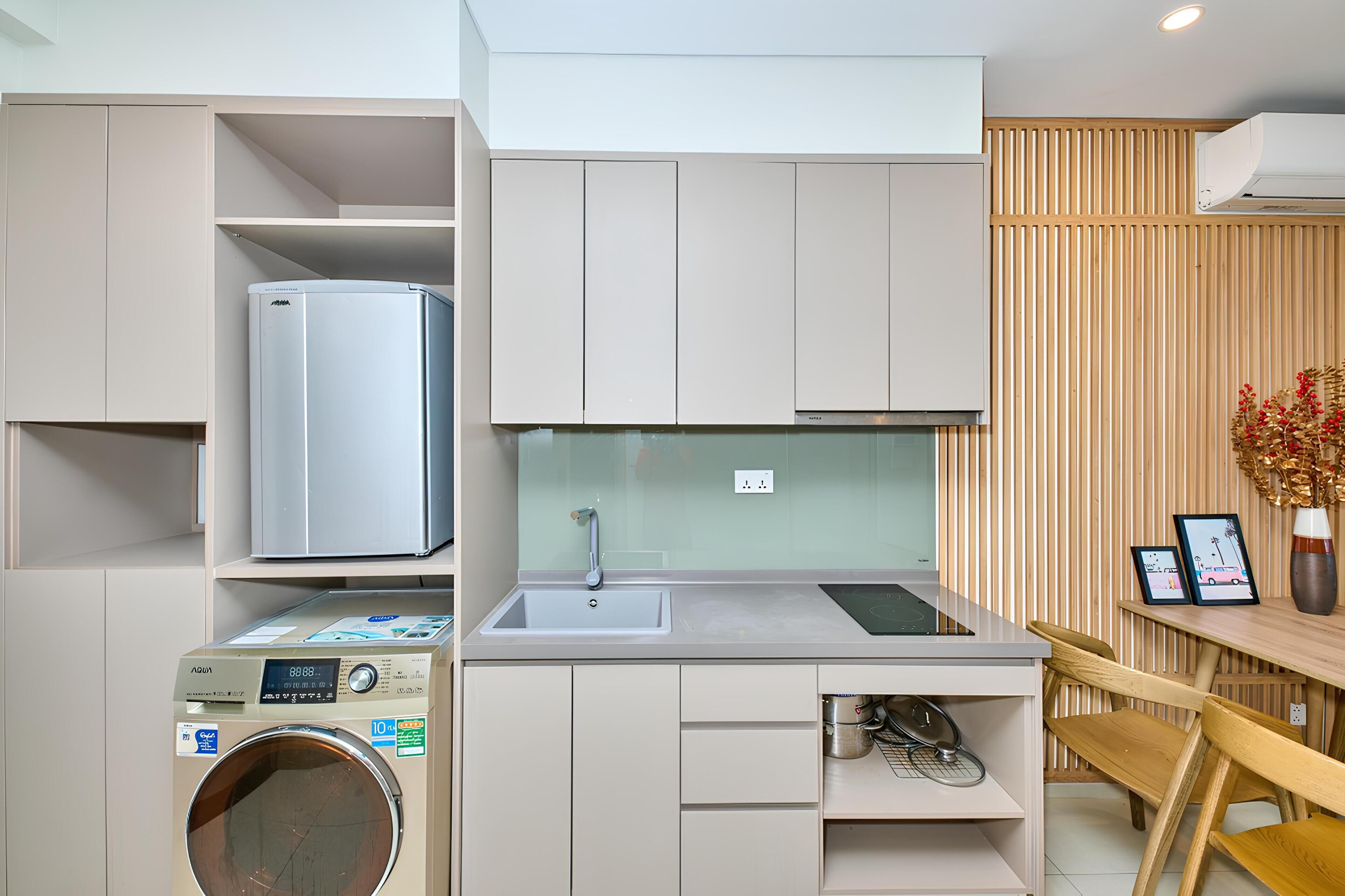 Een compacte keuken met een ingebouwde wasmachine, een spoelbak en een eethoek met een houten tafel.
