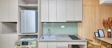 Een compacte keuken met een ingebouwde wasmachine, een spoelbak en een eethoek met een houten tafel.