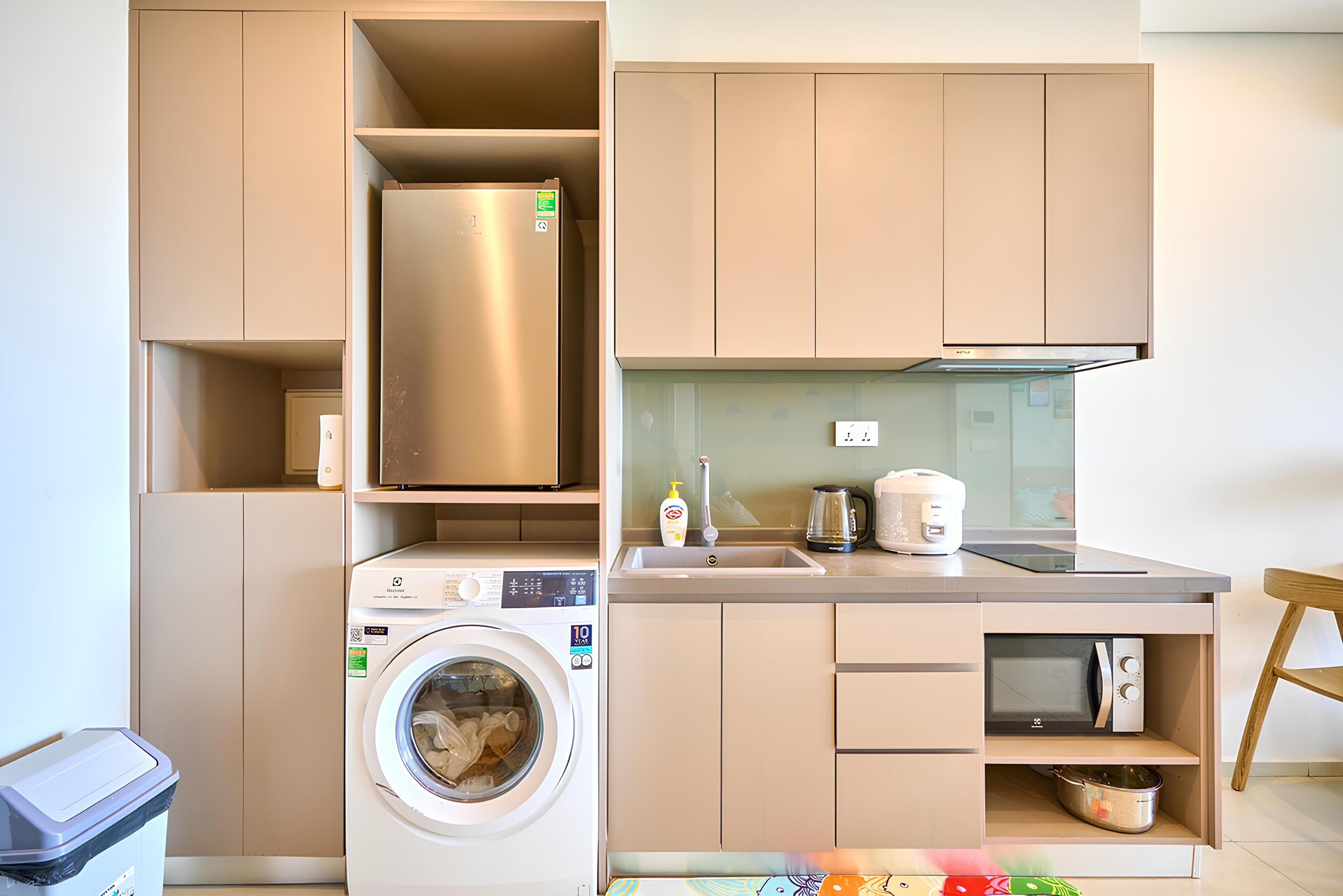 Eine kompakte Küche mit Waschmaschine, Edelstahl-Kühlschrank, Mikrowelle und Spüle.